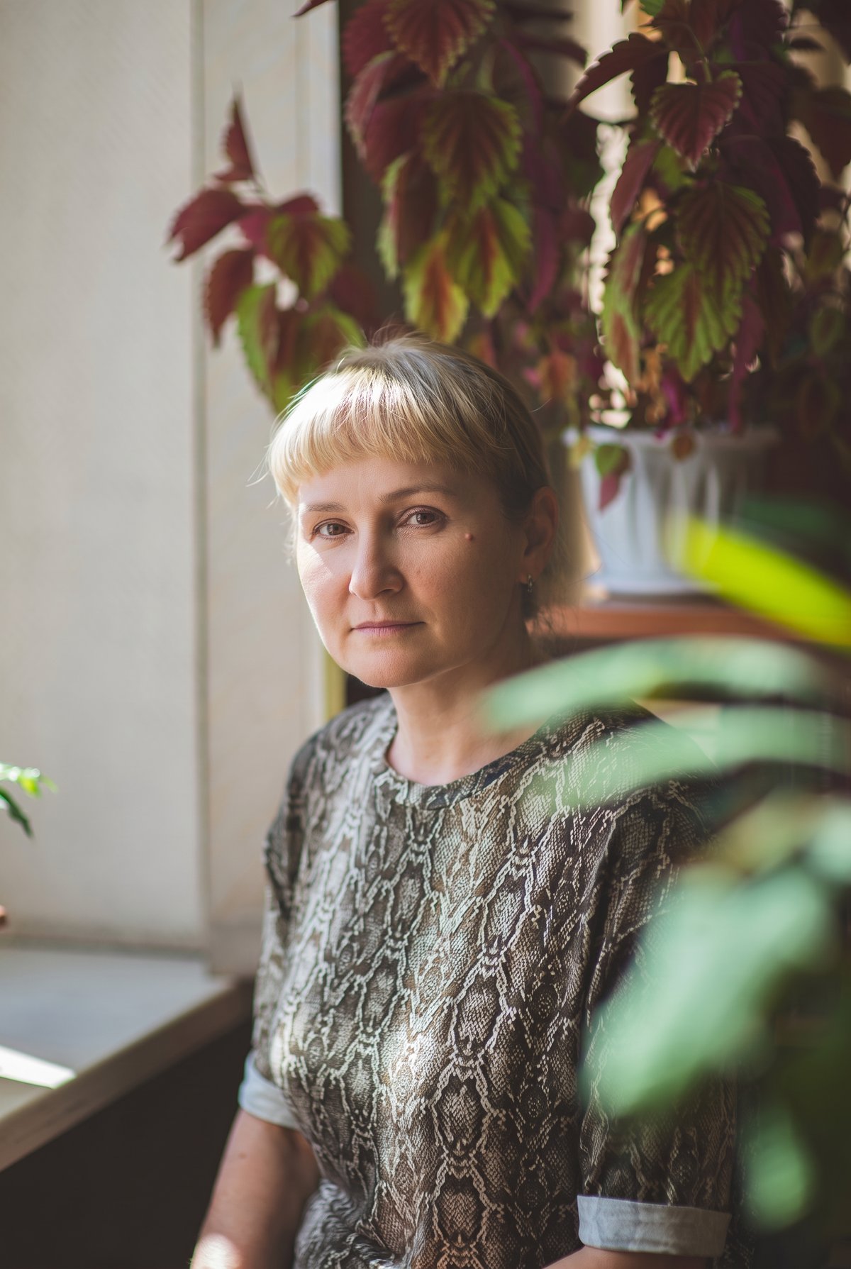 A woman in her sixties sitting calmly among houseplants in warm natural light